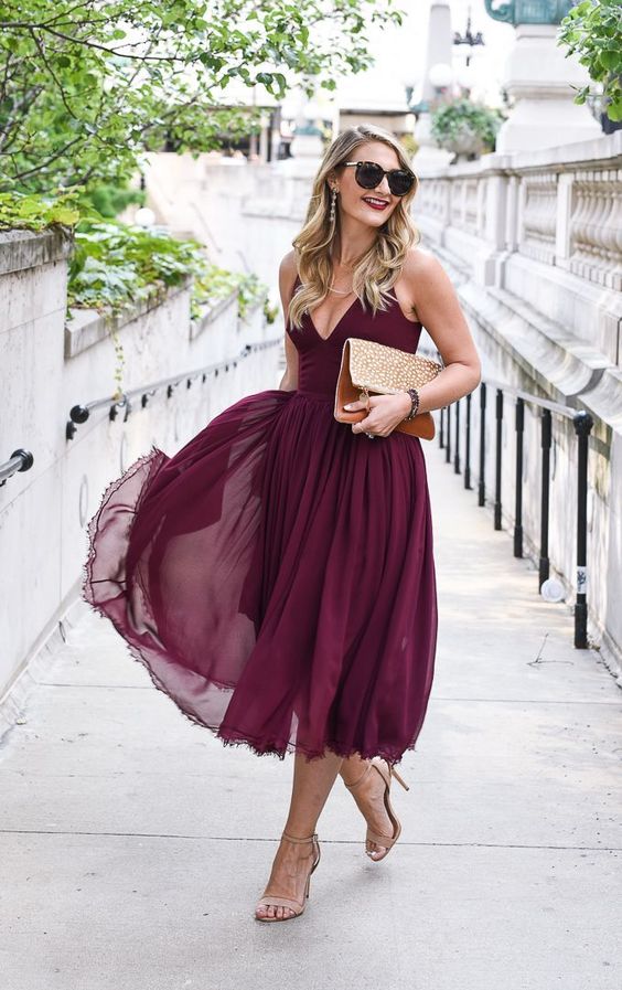 a burgundy A line midi dress with a V neckline, a flowy skirt, nude  shoes and an embellished clutch
