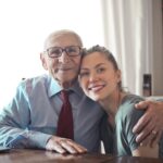 Free Positive senior man in formal wear and eyeglasses hugging with young lady while sitting at table Stock Photo