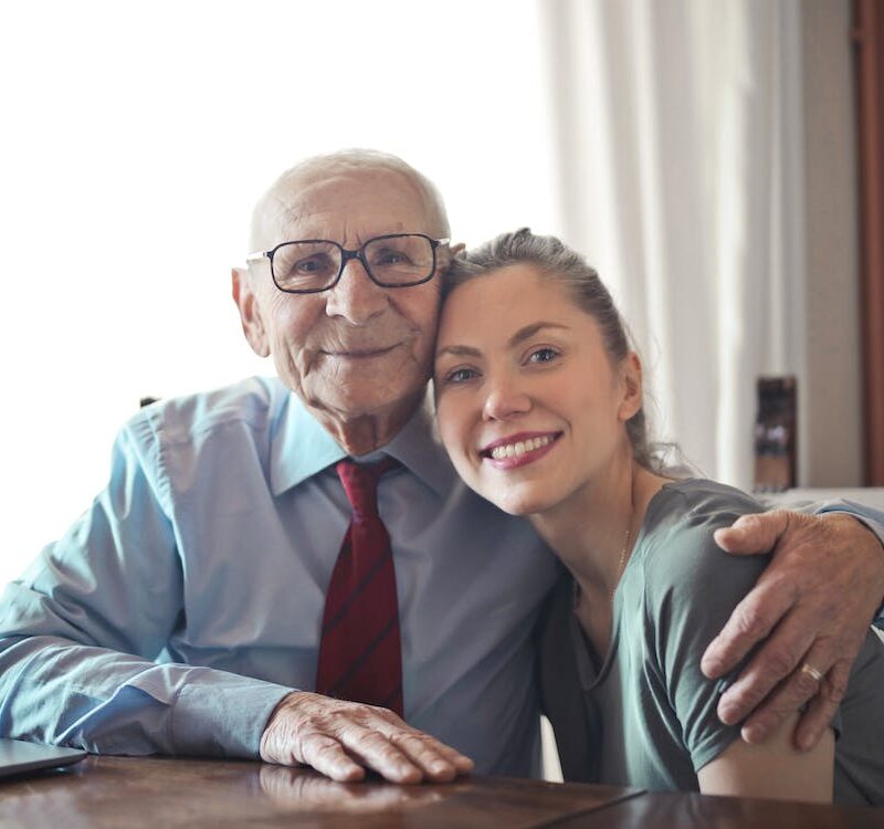 Free Positive senior man in formal wear and eyeglasses hugging with young lady while sitting at table Stock Photo
